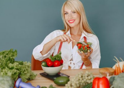 Blonde woman enjoying a fresh salad surrounded by vegetables, promoting healthy eating.