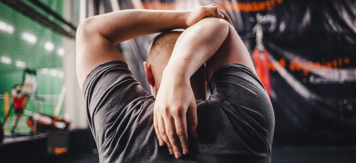 Man stretching arms in a gym, viewed from behind, focusing on fitness and flexibility.