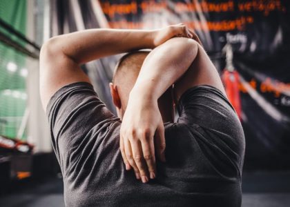 Man stretching arms in a gym, viewed from behind, focusing on fitness and flexibility.