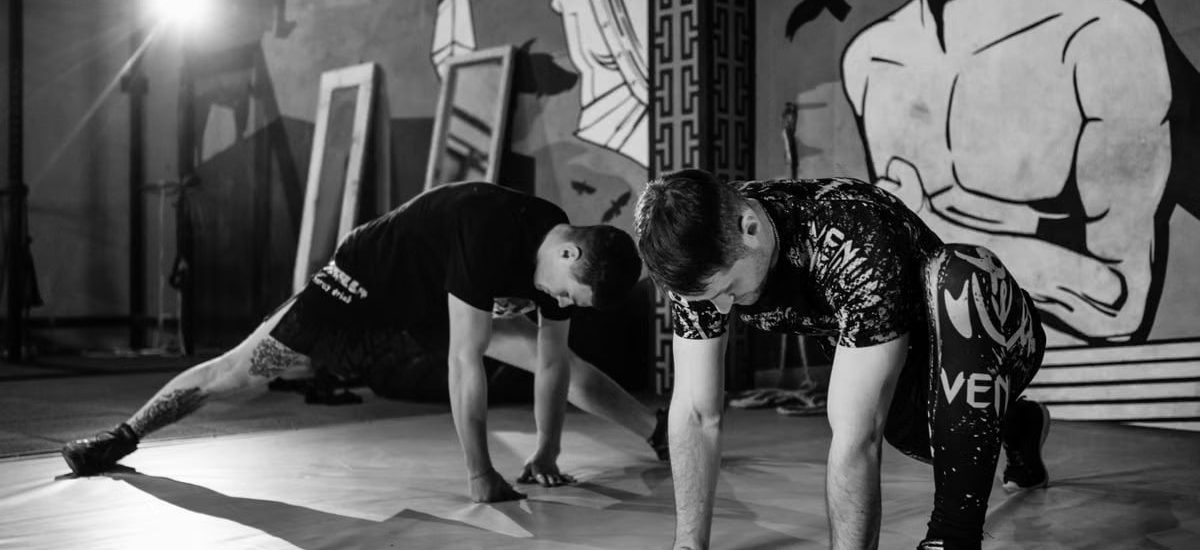 Two men stretching inside a gym, preparing for MMA training in a grayscale setting.