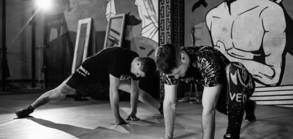 Two men stretching inside a gym, preparing for MMA training in a grayscale setting.