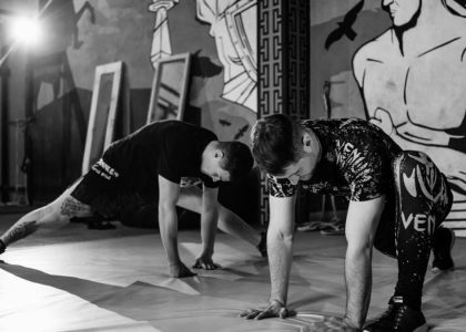Two men stretching inside a gym, preparing for MMA training in a grayscale setting.